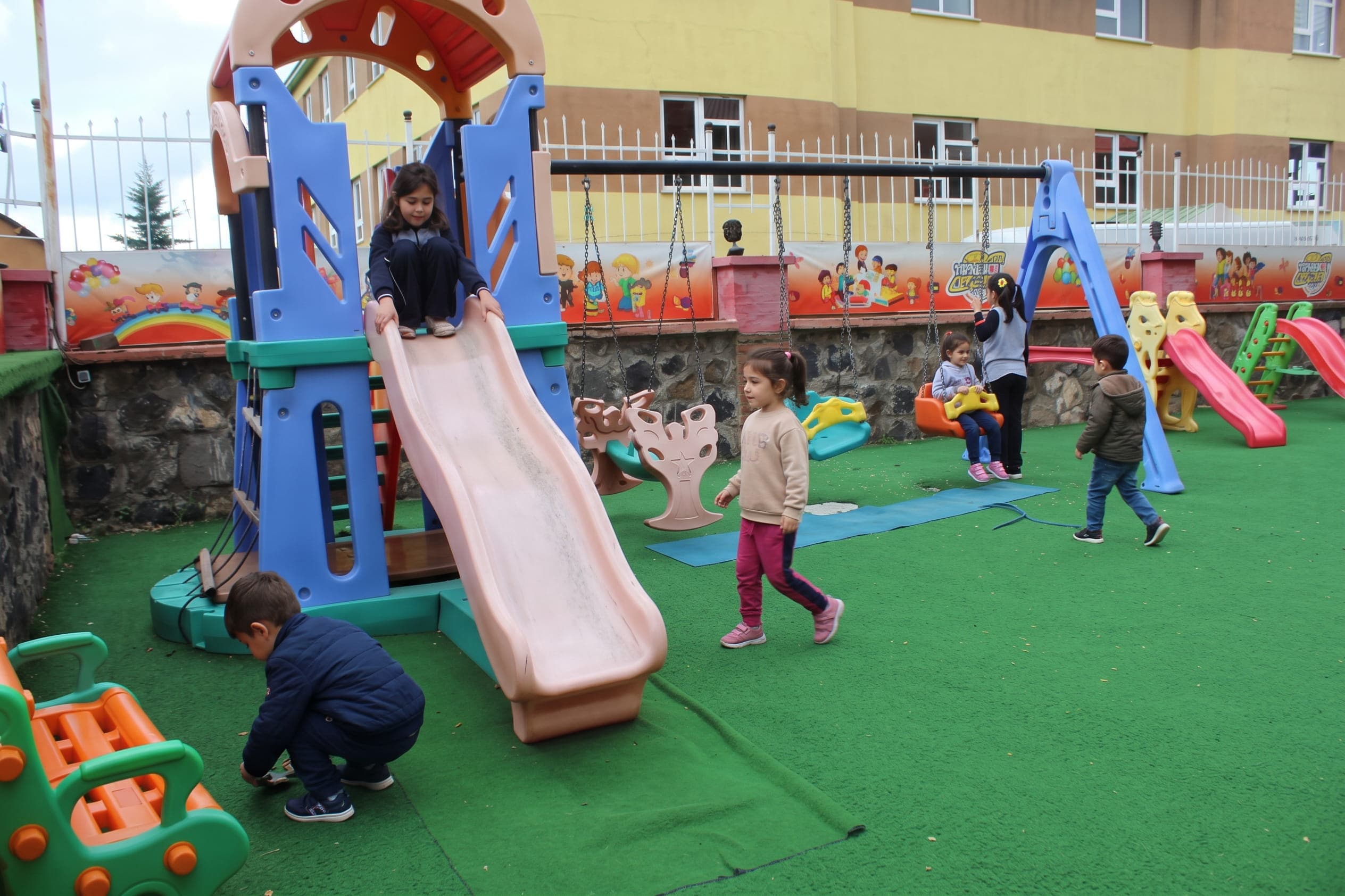 Bahçedeki oyun parkında kaydırak ve salıncakta oynayan çocuklar